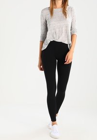 Grå långärmad topp som matchas med svarta leggings; båda i ett stretchigt material. Vita sneakers fulländar outfiten. Enkelt design och passform.