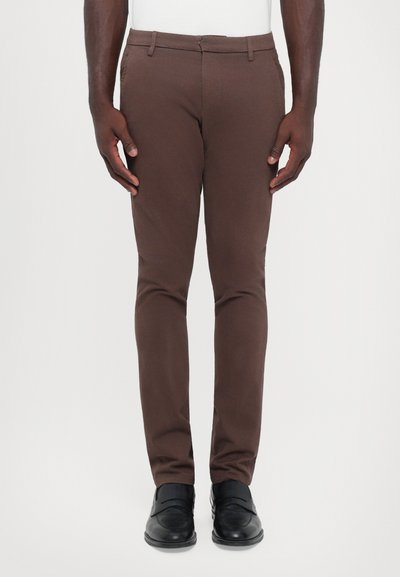 Brown slim-fit trousers made of smooth fabric, featuring a flat front, belt loops, and side pockets, paired with black shoes.