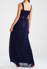 Vestito maxi blu navy con corpetto arricciato, spalline larghe e dettaglio in raso a fiocco in vita. Tessuto fluido con una consistenza trasparente.