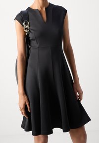 Robe noire à manches courtes en tissu extensible, présentant un décolleté en V et une jupe évasée, avec une texture lisse et des lignes épurées.