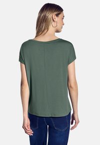 Sako s krátkým rukávem v olivově zelené barvě s kulatým výstřihem a rovnými linemi. Měkká tkanina s hladkým povrchem a čistým zadním švem.