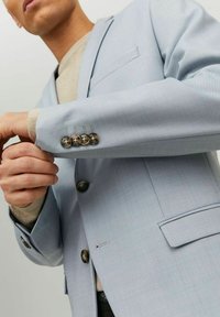 Giacca da abito azzurro chiaro con un tessuto strutturato, caratterizzata da un colletto sciallato, tasca sul petto e cinque bottoni decorativi sul polsino.