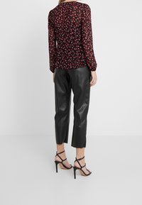 Blouse à imprimé floral noir avec manches longues, coupe ample et détails froncés à l'arrière, associée à un pantalon court en cuir noir et des talons à brides.