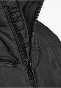 Svart isolert jakke med teksturert overflate, med en tydelig glidelås, brodert logo og en sidelomme med glidelås.