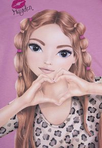 Grafica di una ragazza con lunghi capelli castani mossi, acconciati con fermagli rosa, che indossa una maglietta grigia con stampa leopardata e forma un cuore con le mani.
