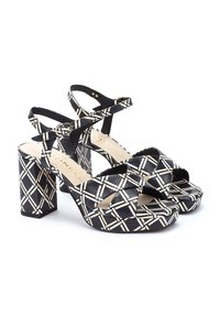 Sandalias de tacón alto en blanco y negro con un tacón bloque grueso, correas en el tobillo y un diseño de tiras cruzadas, con un acabado texturizado.