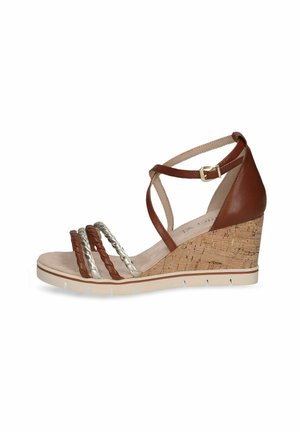 Sandale compensée en cuir marron avec un talon en liège, des brides argentées tressées et une boucle à la cheville. Elle possède un semelle intérieure rembourrée et une semelle blanche.