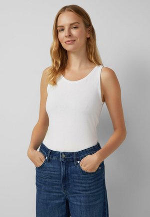 Top bianco senza maniche con scollatura rotonda, realizzato in tessuto morbido. Abbinato a jeans di denim blu scuro con tasche frontali.