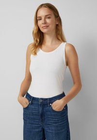 Witte mouwloze top met een ronde halslijn, gemaakt van een gladde stof. Gecombineerd met donkerblauwe denim jeans met voorkeurszakken.