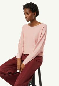 Light pink long-sleeve sweater with a wide neckline, paired with deep burgundy loose-fitting trousers, showcasing soft textures and relaxed design.