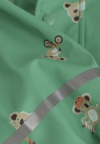 Lys grøn vandtæt stof med tegneserie koalaer i forskellige positurer. Har en sølv refleksiv accentstribe. Blød, glat tekstur.
