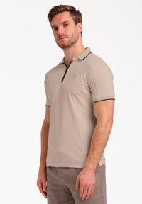 Polo de color beige con mangas cortas, cuello con cremallera y acentos en color marino en el cuello y los bordes de las mangas. Tela suave y ligera.