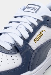 Hvide og blå sneakers lavet af læder og syntetiske materialer, med guldlogo, tekstureret overdel og hvide snørebånd med perforeret tåboks.