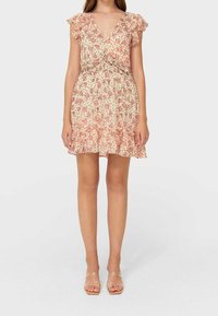 Kukkamekko, jossa on V-pääntie, lyhyet röyhelösateet ja joustava vyötärö. Vaalea kerma tausta vaaleanpunaisella kukkakuviolla ja levenevä helma.