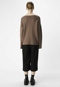 Bruine oversized trui met een ronde hals, gecombineerd met zwarte cropped broeken en stevige zwarte schoenen. Glad textuur.
