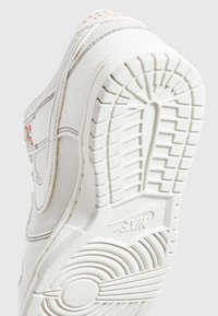 Baskets blanches avec empeigne en tissu texturé, semelle extérieure en caoutchouc présentant un motif rainuré, et un logo discret rouge sur le côté.