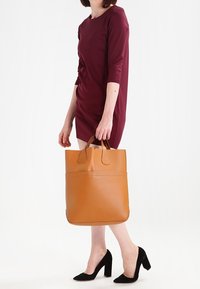 Brun läder tote-väska med dubbla handtag, slät yta, rektangulär form och en framficka. Inga synliga mönster eller hårdvara.