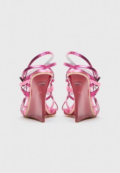Spīdīgas rozā augstpapēžu sandales ar vairākiem siksniņām, skatītas no aizmugures uz vienkārša baltā fona.