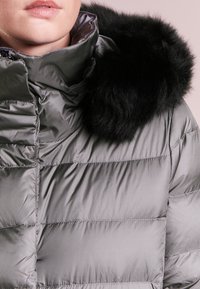 Šedá prošívaná bunda s lesklým povrchem, vybavená černým límcem z umělé kožešiny. Látka má prošívaný vzor a zapínání na zip.