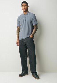 Ljusblå polo med korta ärmar, mörka jeans och svarta skor. Egenskaper inkluderar en klassisk krage och en subtil textur.