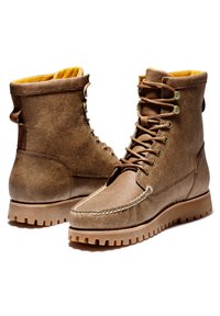 Hnědé kožené boty s texturovaným povrchem, žlutým podšitím, kulatou špičkou a robustní podrážkou s profilováním. Obsahují kovové prostupy a tkaničky s háčky.