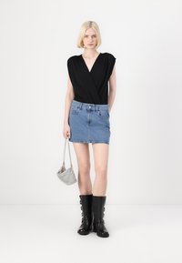Svart omslagsbluse, lyseblå denim miniskjørt, svarte høye støvler med spenner og en liten sølvveske. Enkel, ren design.