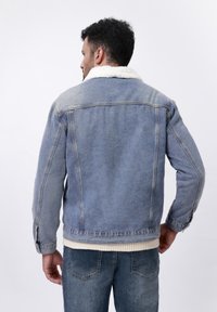 Denimjack met een lichtblauwe wassing, witte fleece kraag en lange mouwen. Heeft een klassieke snit en knoopdetails aan de voorkant.