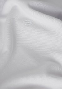 Tejido blanco con un patrón texturizado, que presenta sutiles arrugas y un pequeño logo bordado en hilo blanco a juego.