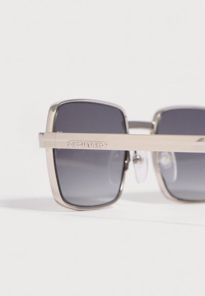 Lunettes de soleil carrées avec montures en métal argenté et verres teintés foncés, avec "DSQUARED2" gravé sur la branche.