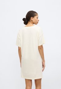 Κοντό ελεφάντινο φόρεμα t-shirt από μαλακό βαμβάκι, με χαλαρή εφαρμογή, ωραίους ώμους και στρογγυλή λαιμόκοψη. Λείο ύφασμα και μήκος έως το γόνατο.