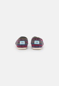 Scarpe slip-on con motivo geometrico multicolore, bordatura nera e suole in gomma di colore chiaro. Logo "TOMS" visibile sul tallone.