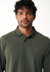 Donkergroene polo met kraag, twee knopen en een subtiele logo op de borst. Duurzaam, zacht stof met een gladde textuur.