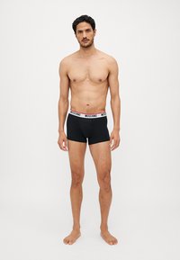 Sorte boksershorts med en hvid og rød MOSCHINO-bælte, der har en tætsiddende pasform og blød tekstur, vist på en model uden skjorte.