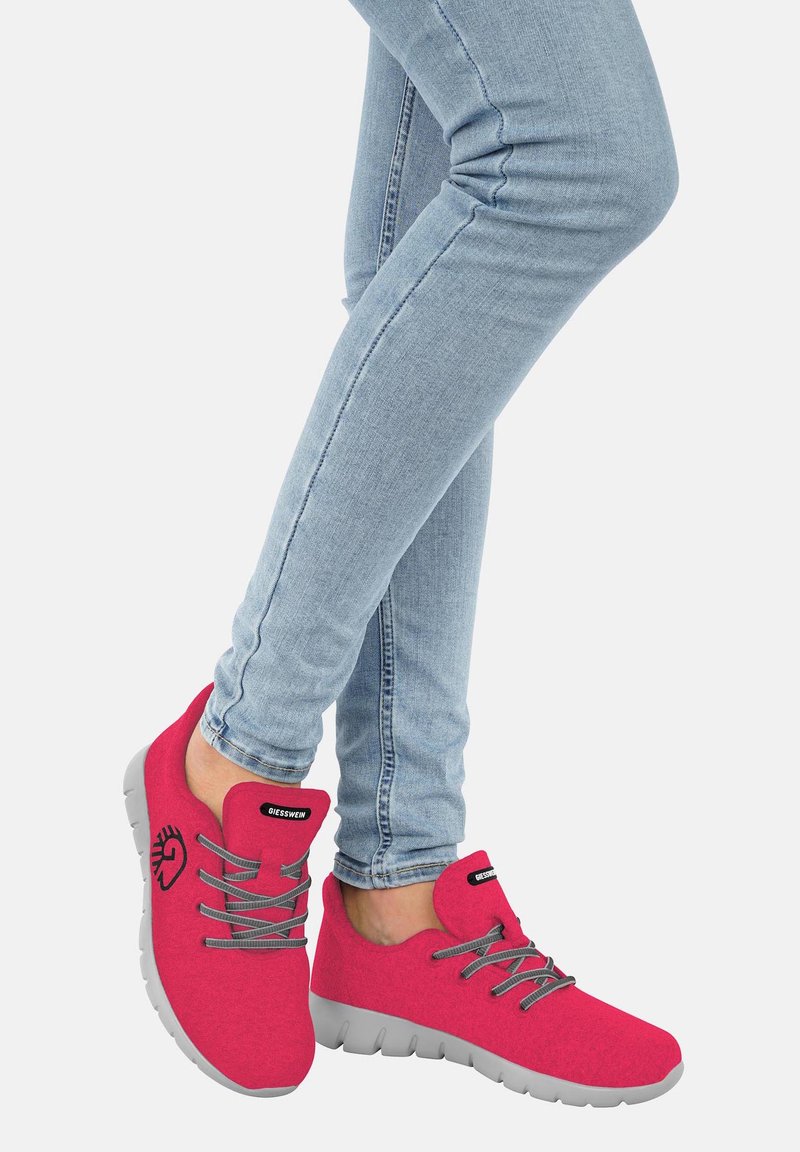 Rote Stoffschuhe mit elastischen Schnüren, grauer Sohle, abgerundeter Spitze und einem kleinen Logoakzent. Getragen mit hellblauen Skinny-Jeans.