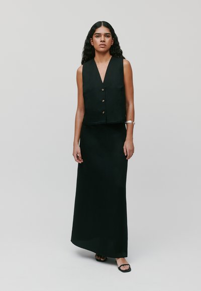 Haut sans manches noir avec un décolleté plongeant et des boutons devant, associé à une longue jupe noire fluide, créant un look monochrome cohérent.