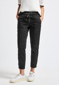 Pantaloni da jogger neri realizzati in tessuto leggero con vita elasticizzata, dettagli con coulisse e orli affusolati; dotati di due tasche laterali.