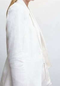 Blazer bianco in lino con vestibilità su misura e revers a punta. Presenta tasche laterali e un design minimalista. Texture liscia.