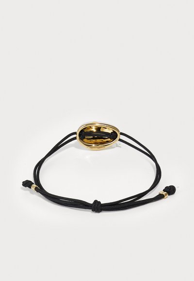 Sort snorarmbånd med en skinnende gul oval lås, der har en glat refleksiv overflade og justerbar længde.