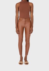 Braunes geripptes Tanktop, eng anliegende braune Leggings aus Kunstleder und beige geflochtene Slidesandalen. Glatte Textur, hoch tailliertes Design, schlanke Silhouette.