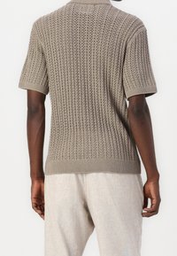 Kortärmad stickad tröja i ljusbrun, med ett mönster av textur, ribbade manschetter och rundad halsringning.