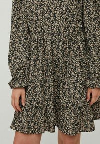 Blommig klänning i mörkgrön tyg med rosa och beige blommor. Har långa ärmar, en indragen midja och fåll med lager.