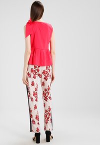 Czerwony top z peplum na lewym ramieniu, połączony z białymi spodniami w kwiaty z czerwonymi wzorami i czarnymi paskami po bokach. Czarne sandały na obcasie.