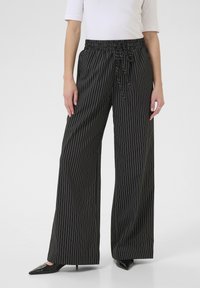 Wide-leg, black striped trousers with a drawstring waist. Smooth fabric with vertical white pinstripes. Flat front and side pockets.