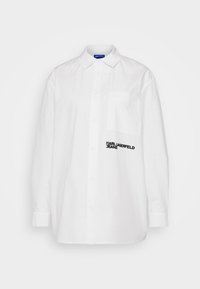 Biała koszula z guzikiem i kołnierzykiem, z kieszonką oraz czarnym logo tekstowym "KARL LAGERFELD JEANS" na lewej piersi. Gładka tekstura.