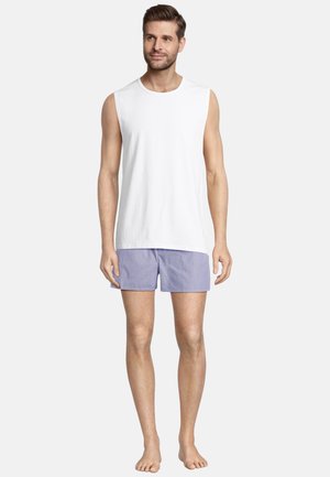 Witte mouwloze shirt van zachte stof, gecombineerd met lichtpaarse gestreepte shorts. Model staat blootsvoets tegen een effen achtergrond.