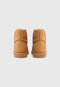 Botins de tornozelo castanhos com um acabamento em camurça suave, apresentando costuras reforçadas, um salto baixo e um interior suave. Sem logótipos visíveis.