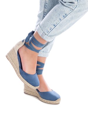 Cuñas de ante azul con suela de yute trenzado, lazos en el tobillo y diseño de punta redonda. Llevadas con jeans de mezclilla clara remangados.