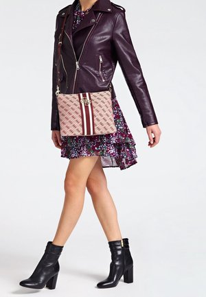 Personne portant une robe fleurie violette, une veste en cuir violet foncé, des bottines noires et un sac bandoulière beige à motifs avec des rayures bordeaux.