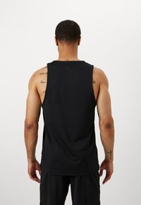 Débardeur noir sans manches en tissu texturé, avec un col rond et une coupe décontractée. La vue de dos montre des détails sur les épaules et le haut des bras.