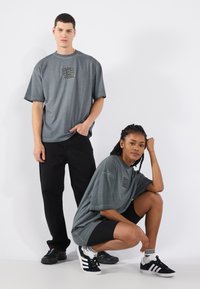 Graue übergroße T-Shirts mit Frontdruck, kombiniert mit schwarzen Hosen und Shorts. Schwarze Schuhe, strukturiertes Material, lässiger Schnitt, entspanntes Design.